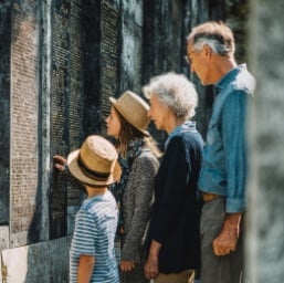 A family stands together in front of a columbarium wall, reading inscriptions and paying their respects in a quiet outdoor setting. The image complements What Visiting a Columbarium Feels Like: A Guide for First-Time Visitors and reflects the peaceful environment often experienced in cemeteries in Schenectady, NY.