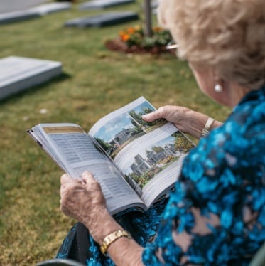 Elderly woman in a cemetery reading a brochure with headstones and memorial plots in Schenectady, NY.